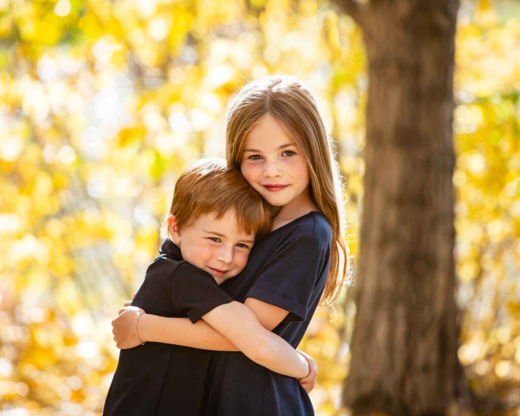 siblings hugging in yellow leaves